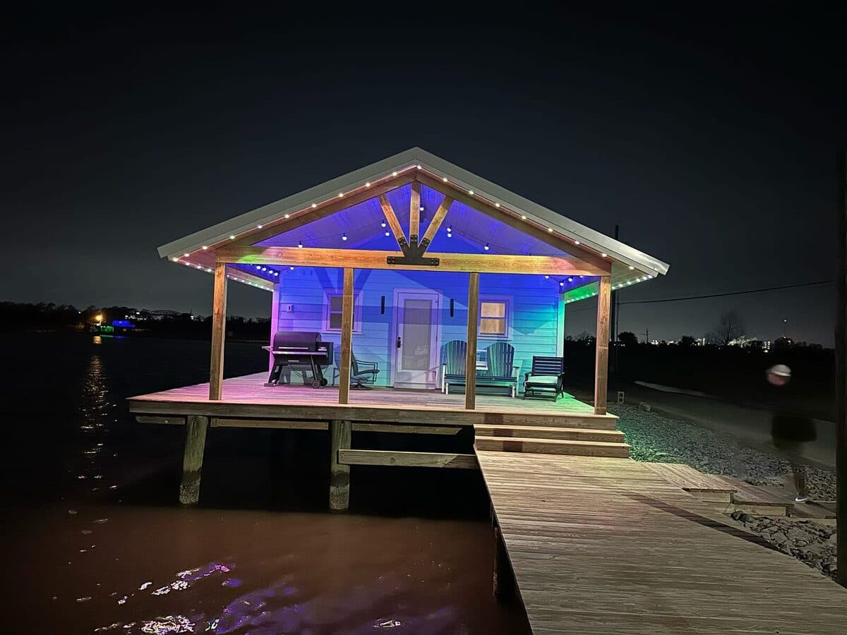 Lakeside cabin at night with GeauxTrax tracks along the porch gable and eaves, lit in rainbow color scene