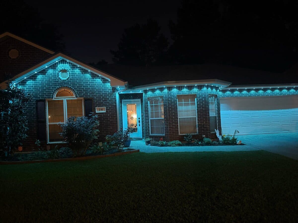 Brick ranch home at night lit in solid teal along the roofline