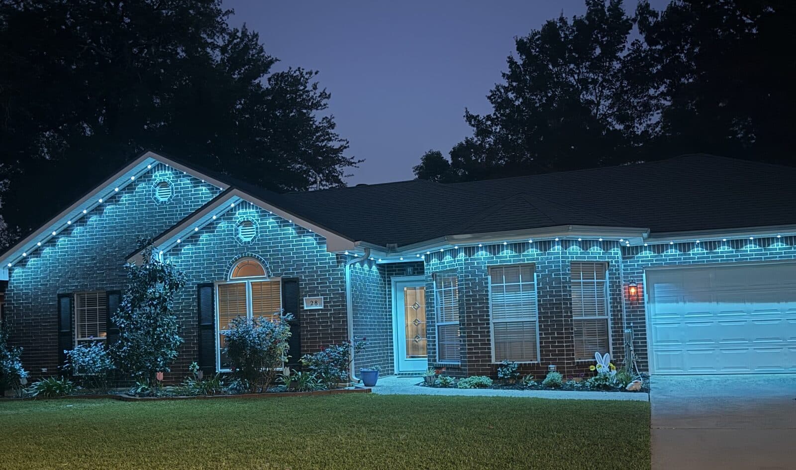 Same brick home at night with GeauxTrax-mounted Govee Permanent Outdoor Pro lights set to a solid teal color scene