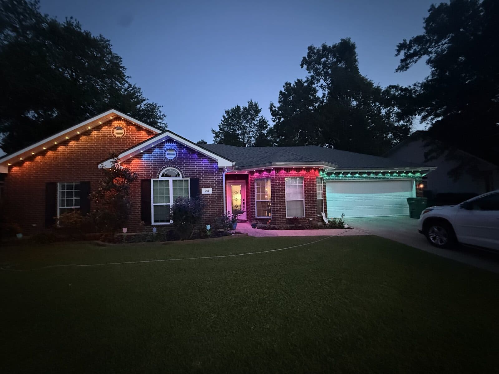 Same brick home with Govee Permanent Outdoor Pro lights in a multi-color scene — magenta over the front door, green over the garage — all wires hidden by GeauxTrax PETG track